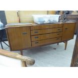 A mid 20thC teak finished sideboard with four central drawers, flanked by a pair of doors,