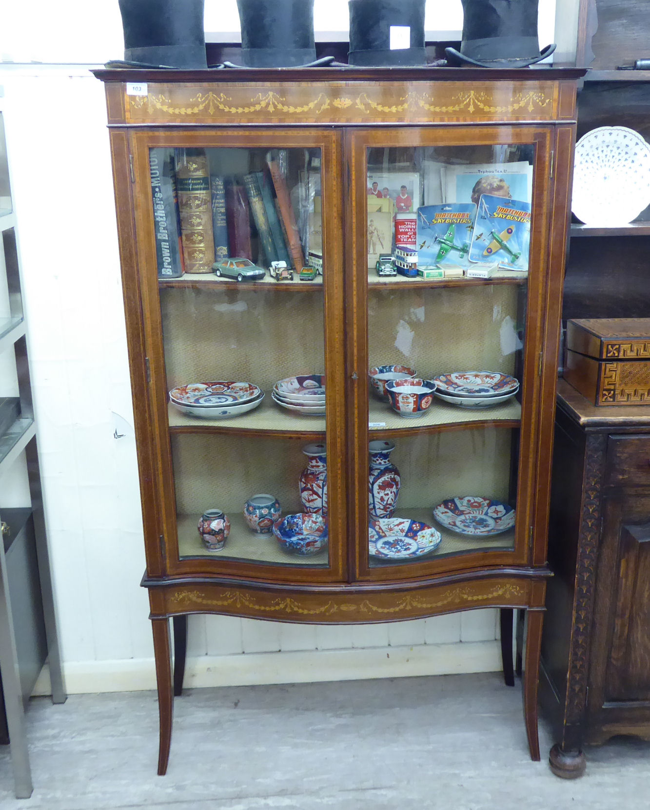 An Edwardian satinwood inlaid mahogany serpentine front display cabinet with a pair of doors,