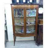 An Edwardian satinwood inlaid mahogany serpentine front display cabinet with a pair of doors,