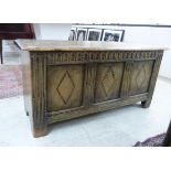 A mid 20thC carved light oak coffer with a tri-panelled front and hinged lid,