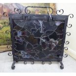 An early 20thC black painted wrought iron firescreen with scrolled ornament,