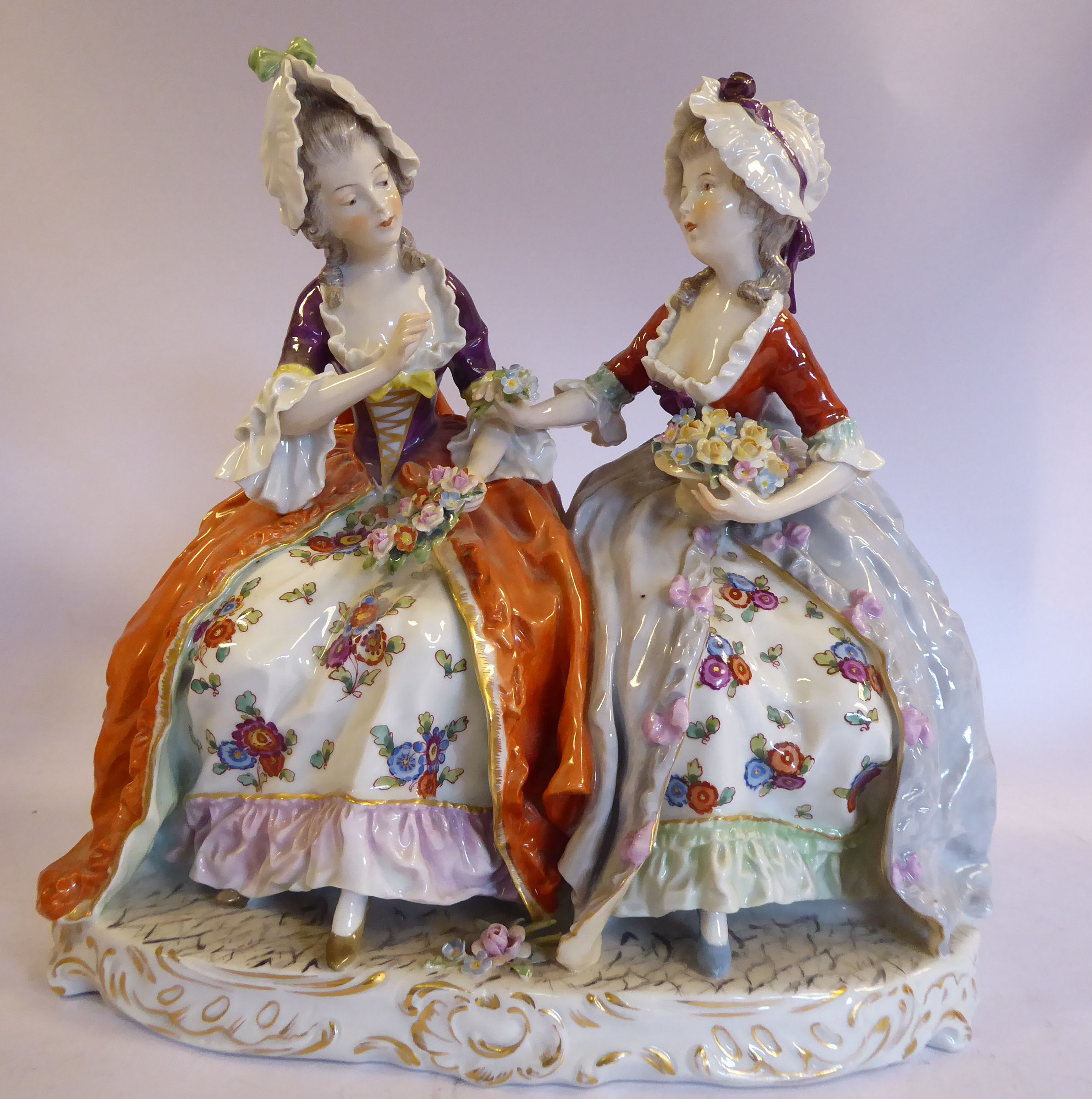 A 20thC Naples porcelain group, two seated young women wearing bonnets and floral skirts,