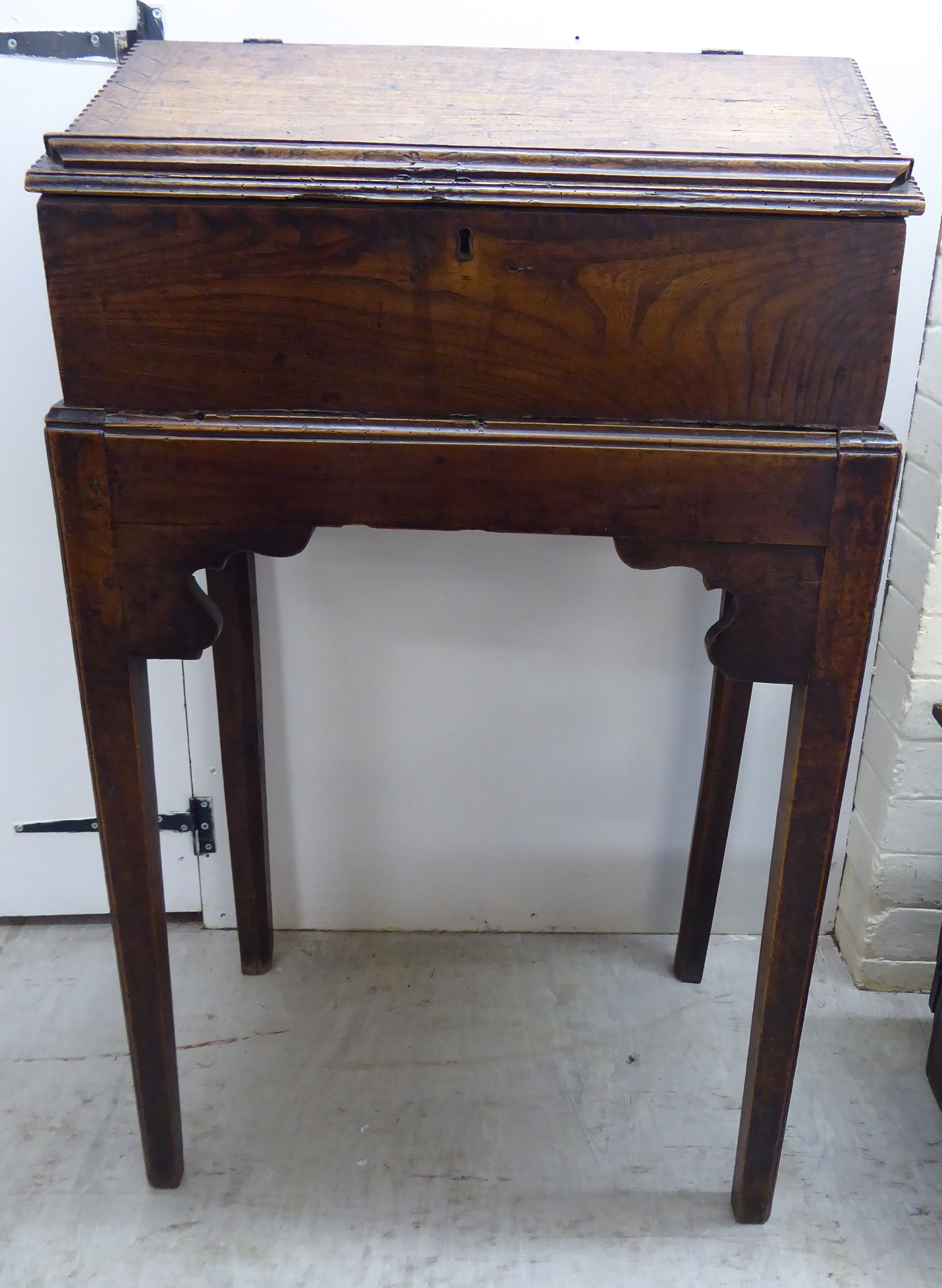 An early George III elm Bible box, on a stand with a hinged, sloping flap, raised on square,