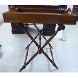 A late 19thC walnut butler's tray with opposing cut-out handles, set on a folding, crossover,