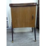 A 1960s teak finished cabinet with a rising table top and a cupboard,