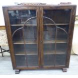 A 1930s oak display cabinet, enclosed by a pair of full-height, glazed panelled doors,