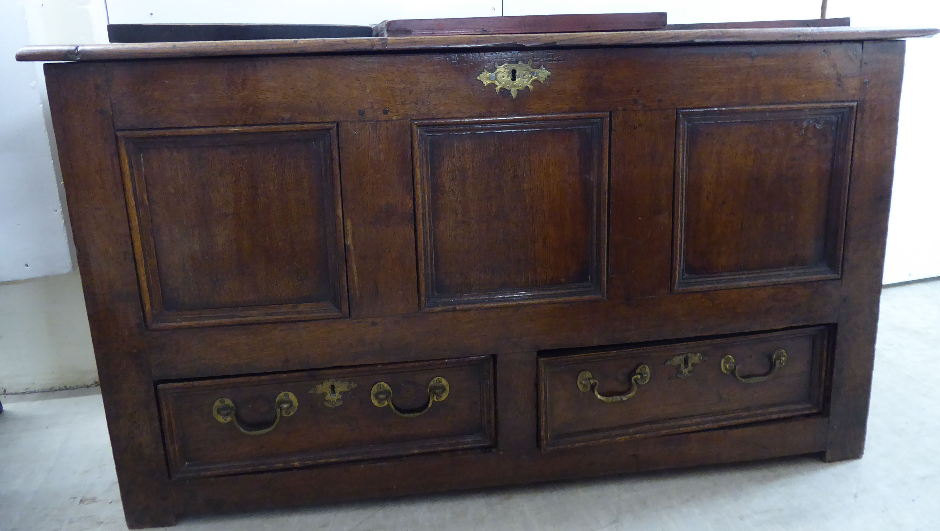 A late 18thC oak coffer with a hinged lid, over a tri-panelled front and two frieze drawers,