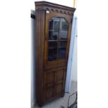 A modern reproduction of an Old English style stained oak corner cabinet with a glazed door,