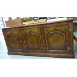 A modern reproduction of an Old English style stained oak sideboard with three panelled doors,