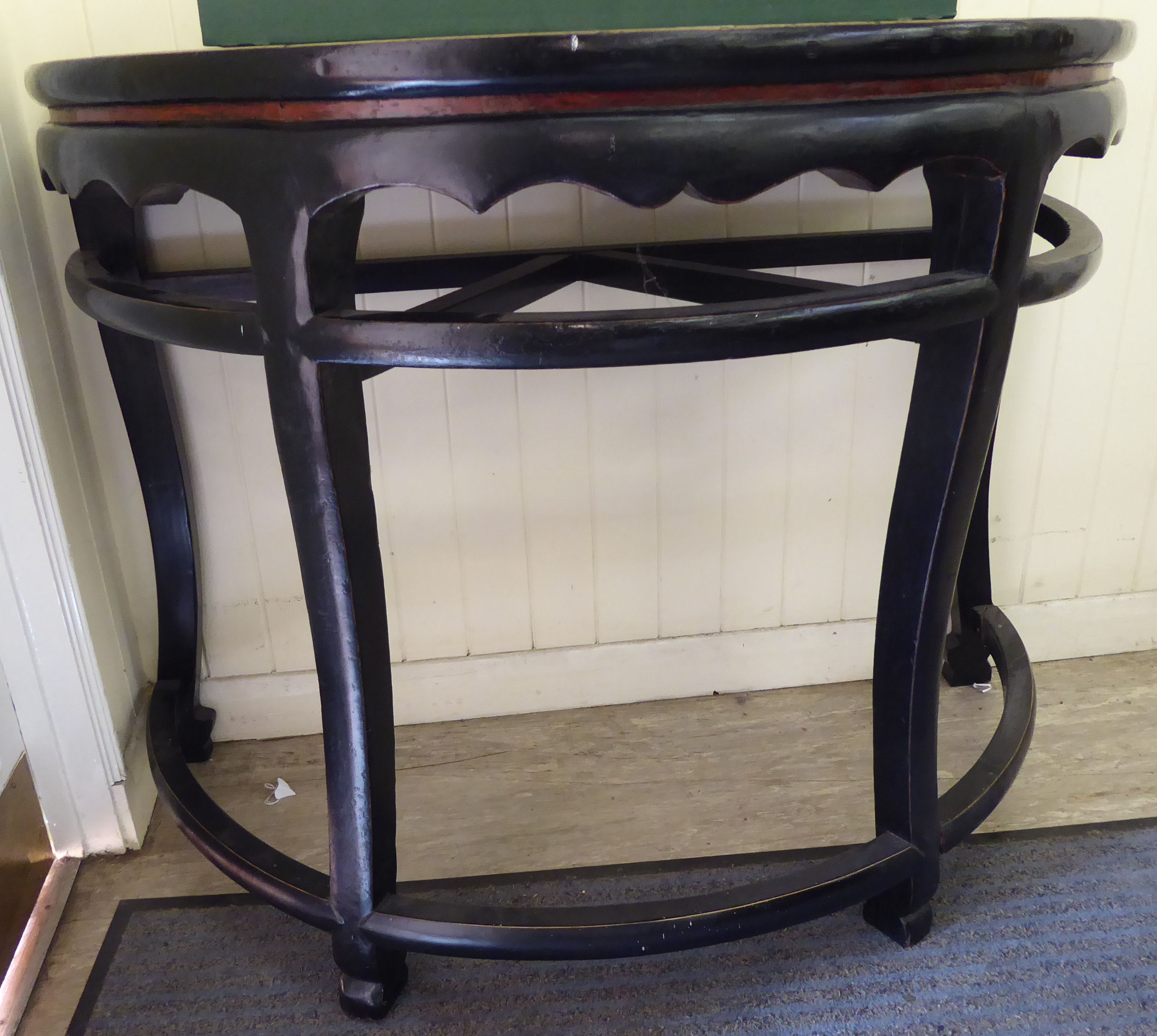 A 20thC Chinese black and iron red lacquered elm D-shaped console table with a wavy edged apron,