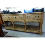 A rustically constructed pine dresser with three in-line drawers, raised on turned pillar supports,