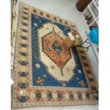 A Persian design woollen rug with a central gul on a blue and terracotta ground 96'' x 132''