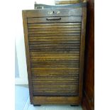 A 1920s light stained oak filing cabinet with a rising tambour front, enclosing file drawers,