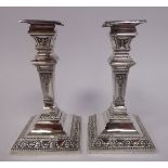 A pair of late Victorian loaded silver neo-classical design candlesticks of square outline,