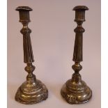 A pair of white metal candlesticks, each with a reed moulded socket, over a floral embossed,