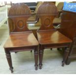 A pair of William IV mahogany framed hall chairs, each with a shell carved back,