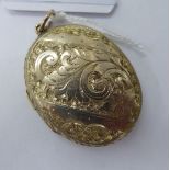 A mid Victorian gold coloured metal oval locket with C-scrolled and foliate engraved ornament