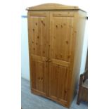 A modern pine wardrobe with a pair of panelled doors, enclosing an open shelf and a hanging rail,