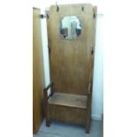 A 1930s oak hall stand, the panelled back with a canted mirror and six hooks, over a hinged seat,