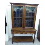 A 1930s stained oak cabinet, the superstructure with a pair of glazed doors,