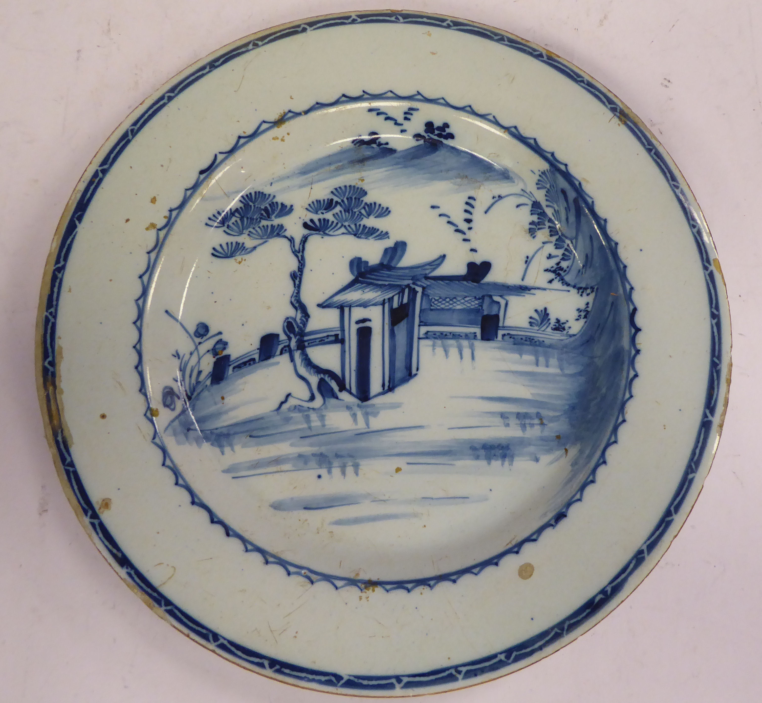 A late 18thC Chinese porcelain broad rimmed plate, decorated in blue and white with a building,