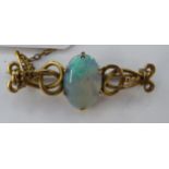 A gold coloured metal scrolled wire framed brooch, claw set with an oval opal,
