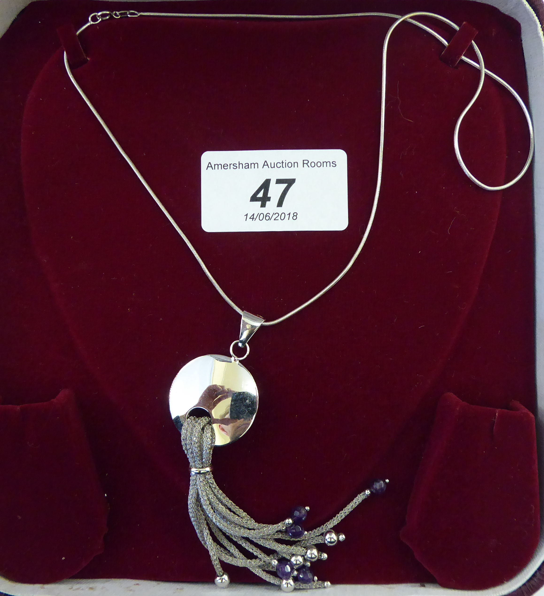 An 18ct white gold pendant necklace, comprising a disc with tassels,