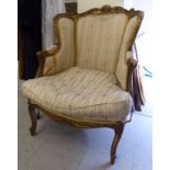 A late 19thC French moulded and carved giltwood, showwood framed chair with a high wing back,