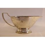 A silver sauce boat of panelled, oval form with an everted lip and an angular wire handle,