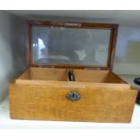 A 1920s light oak cigar box with straight sides and a hinged bevelled clear glass panelled lid,