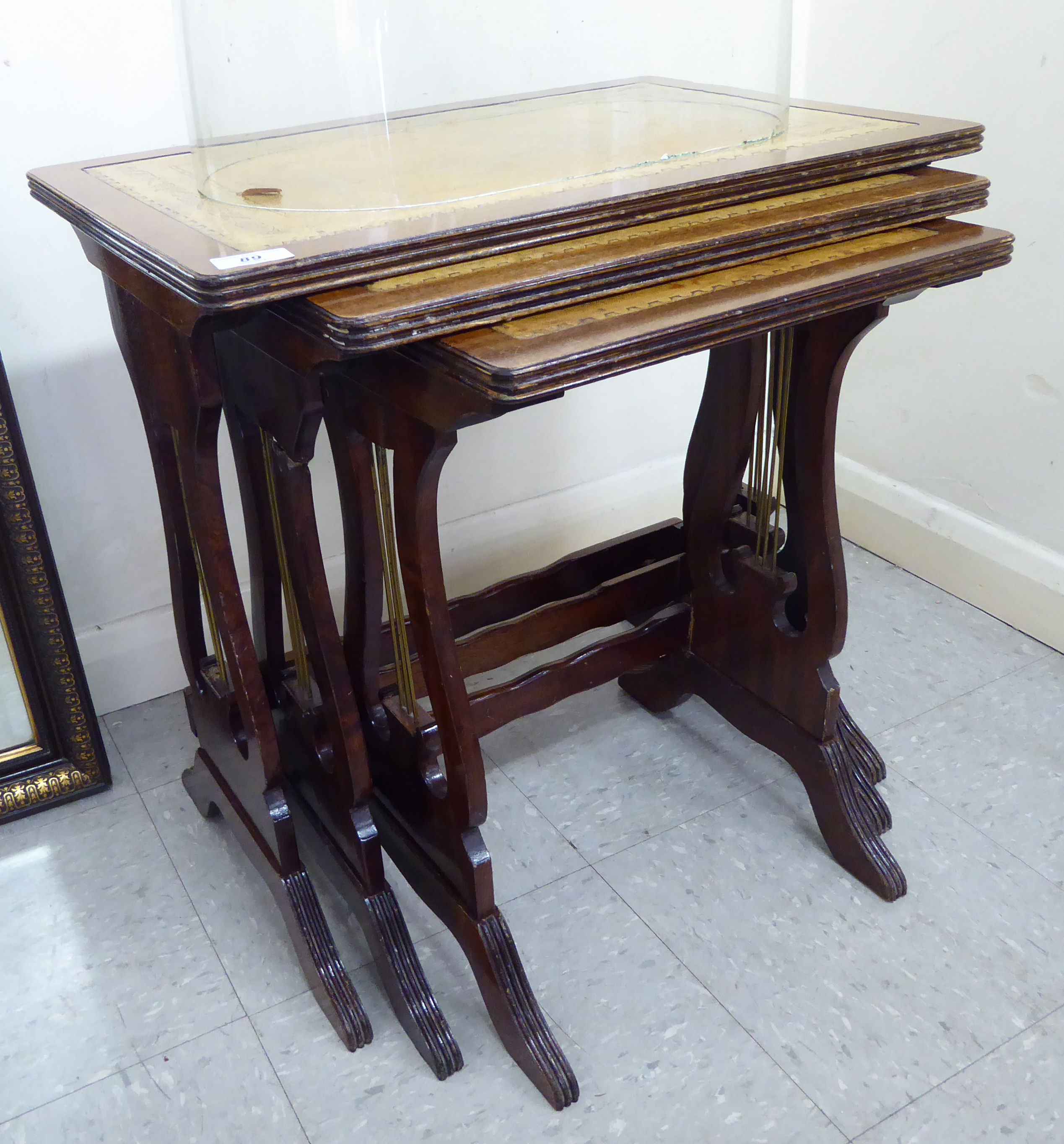 A modern nesting set of three mahogany finished tables with tooled old gold coloured hide surfaces,