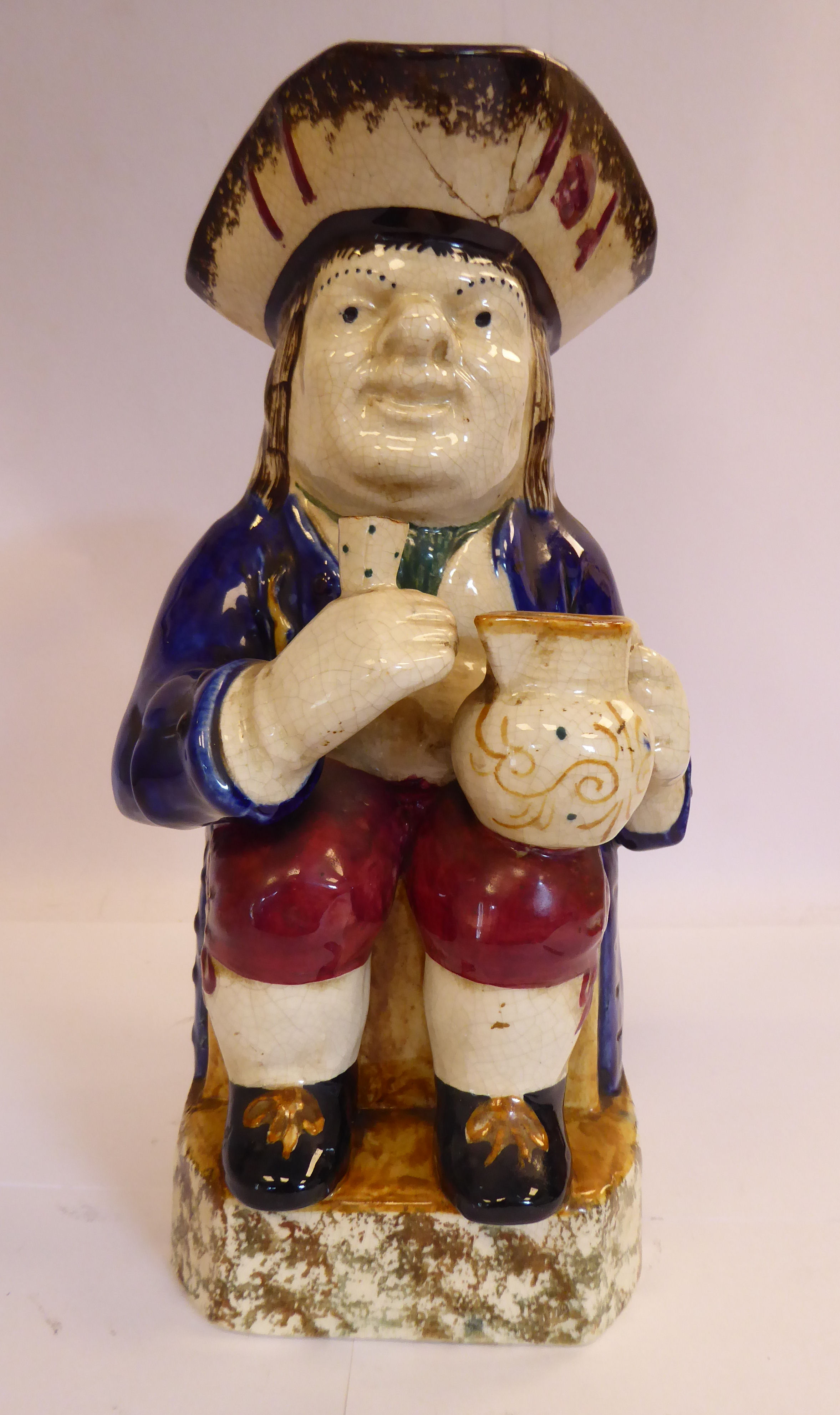 An early 19thC Staffordshire pottery Toby jug, the seated figure wearing a tricorn hat,