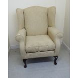 A mid 20thC Georgian design wingback armchair, upholstered in beige foliate fabric,