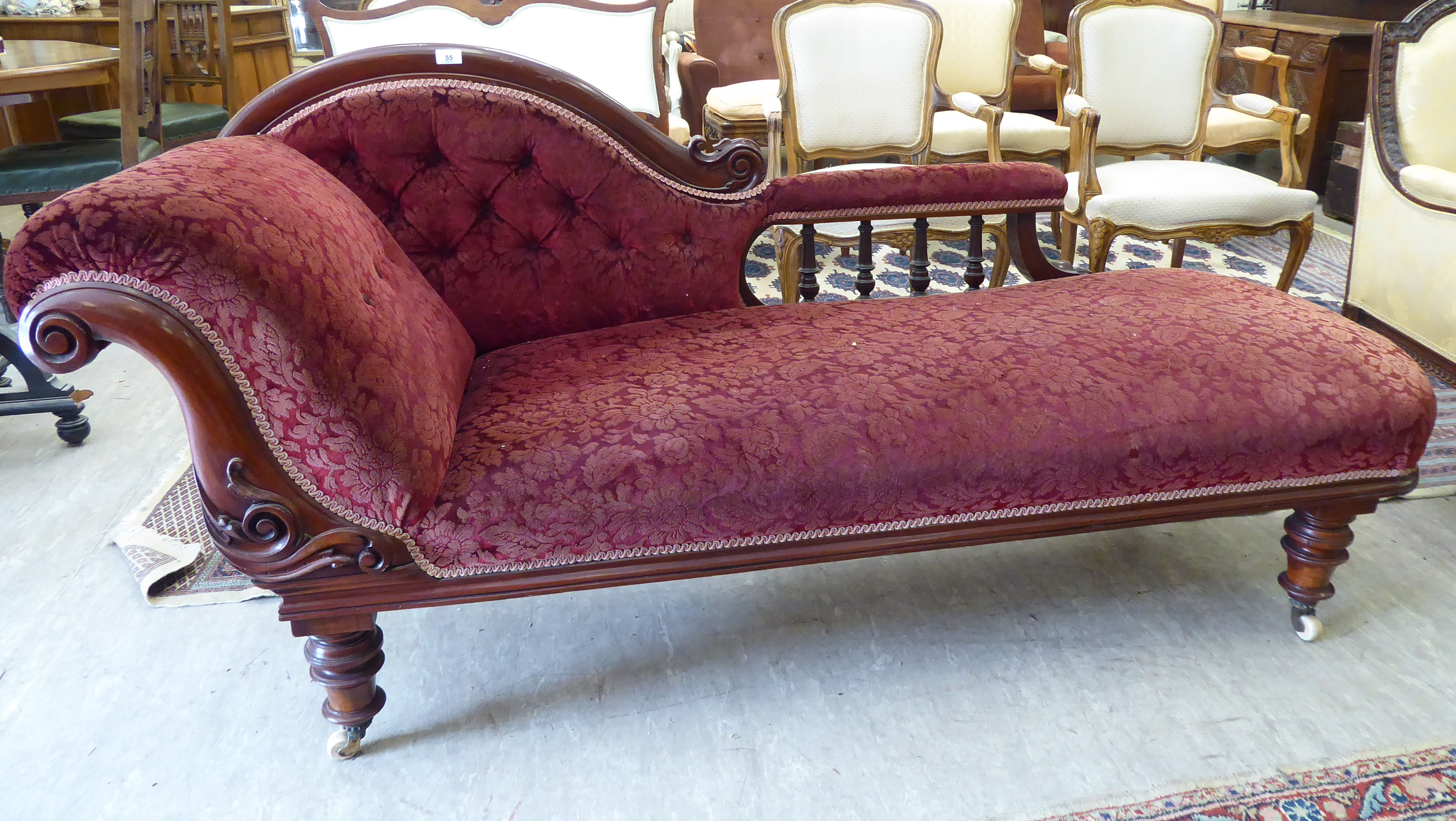 A late Victorian mahogany framed chaise longue, upholstered in a maroon floral fabric,