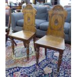 A pair of 1920s oak hall chairs with shell carved panelled backs, over solid seats,