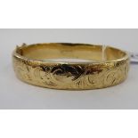 A 9ct gold hollow hinged bangle with bright-cut foliate scrolled ornament,