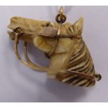 A carved ivory and yellow metal harnessed horses head pendant
