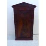 An early Victorian mahogany hanging cupboard with a low, pointed arched cornice, over a lockable,