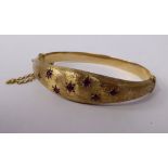 A 9ct gold part textured, hollow, hinged bangle, set with equidistantly spaced rubies,