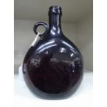 A 19thC semi-opaque dark amber coloured glass wine bottle of flattened form with a strap handle and