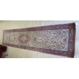 A Persian silk and wool runner with dense floral decoration on a beige and red ground 124'' x 31''