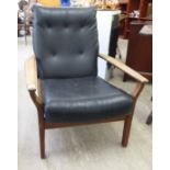 A 1970s teak framed open arm chair, the part button upholstered black faux hide back and seat,