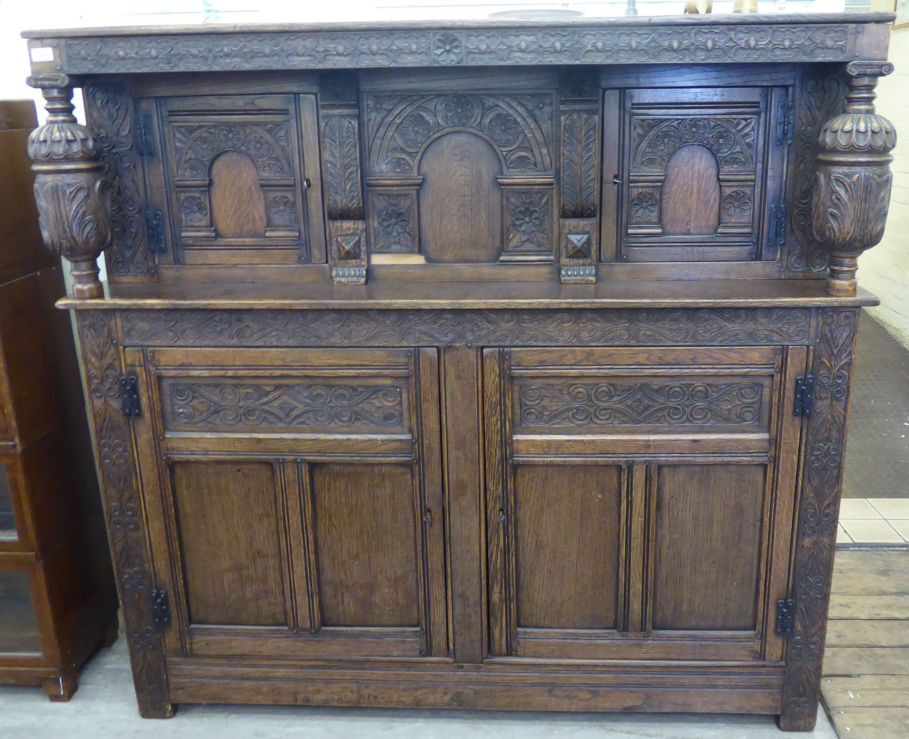 A mid 20thC Jacobean inspired, profusely carved and panelled oak court cupboard with a shelf top,