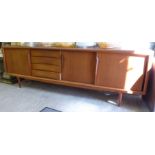 A 1970s teak sideboard with three sliding doors and four drawers,