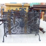 An early 20thC wrought iron firescreen with a mesh back, twin C-scrolled and arrowhead ornament,