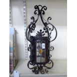 An early 20thC wrought black painted metal hanging lantern with clear and coloured lead glazed