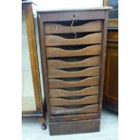 A 1920s stained oak pedestal filing cabinet, the rising tambour front enclosing nine drawers,