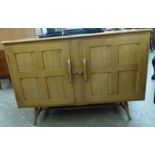 An Ercol elm and beech sideboard with a pair of panelled doors, raised on turned, tapered,