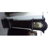 A 1930s stained oak cased granddaughter clock; the movement faced by a brass Roman dial,