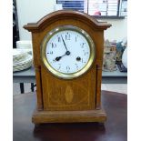 An early 20thC German light oak cased mantel clock with a low, round arched top, over flank pillars,